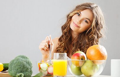 A woman sitting at the table with fruits and vegetables.