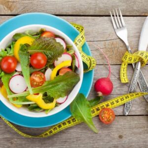 A bowl of salad with vegetables and measuring tape.