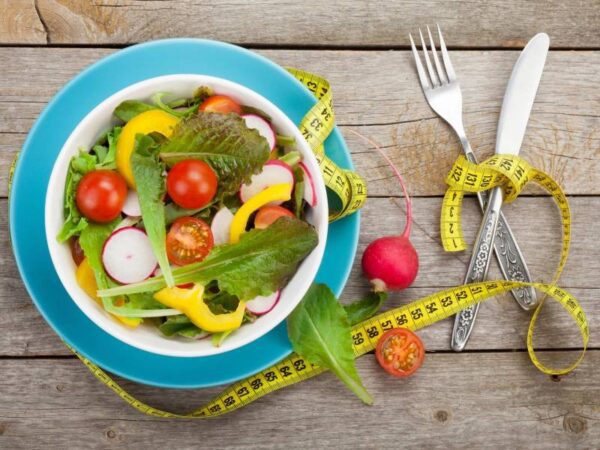 A bowl of salad with vegetables and measuring tape.