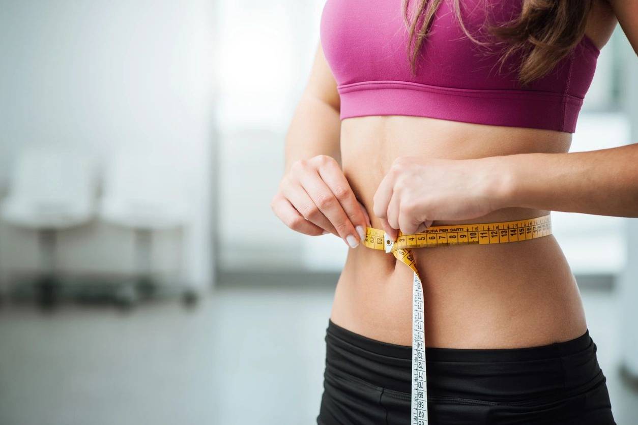 A woman is measuring her waist with a tape measure.